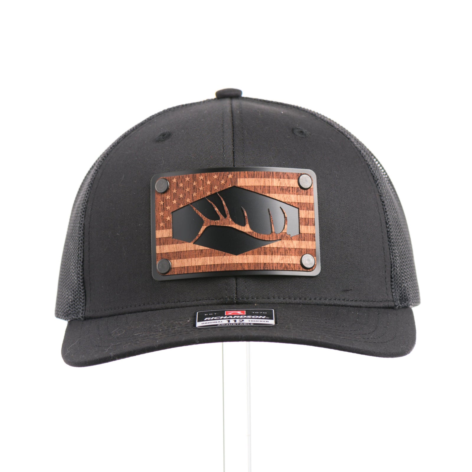 Front of Mahogany Wood Tines American Flag Patch Trucker Hat, featuring a real walnut wood veneer patch etched with an American flag and cut-out elk antler tines, laminated to a black anodized aluminum plate and riveted to an all-black Richardson 112 trucker hat along—handmade in Montana, USA by Last Best Supply Co.