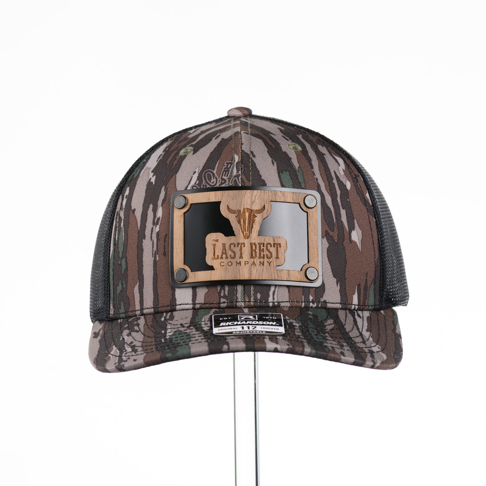 The Last Best Company Original Wood Patch Hat on Realtree Camo Richardson Hat, featuring a real wood veneer patch of The Last Best Company logo riveted to a camo trucker hat along with a metal plate—handmade in Montana, USA by Last Best Supply Co.