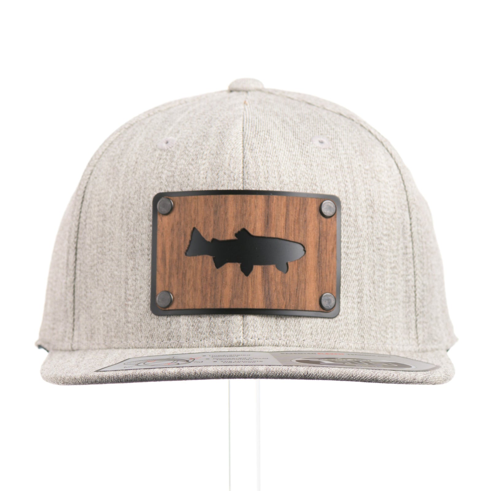The front of a Walnut Trout Patch Plate Heather Grey Flat Bill Hat, featuring a rectangular real walnut wood veneer patch with cut-out trout silhouette, laminated to a black anodized metal plate, and riveted to a light heather grey 6-panel Flexfit Flat Bill Hat—handmade in Montana, USA by Last Best Supply Co.