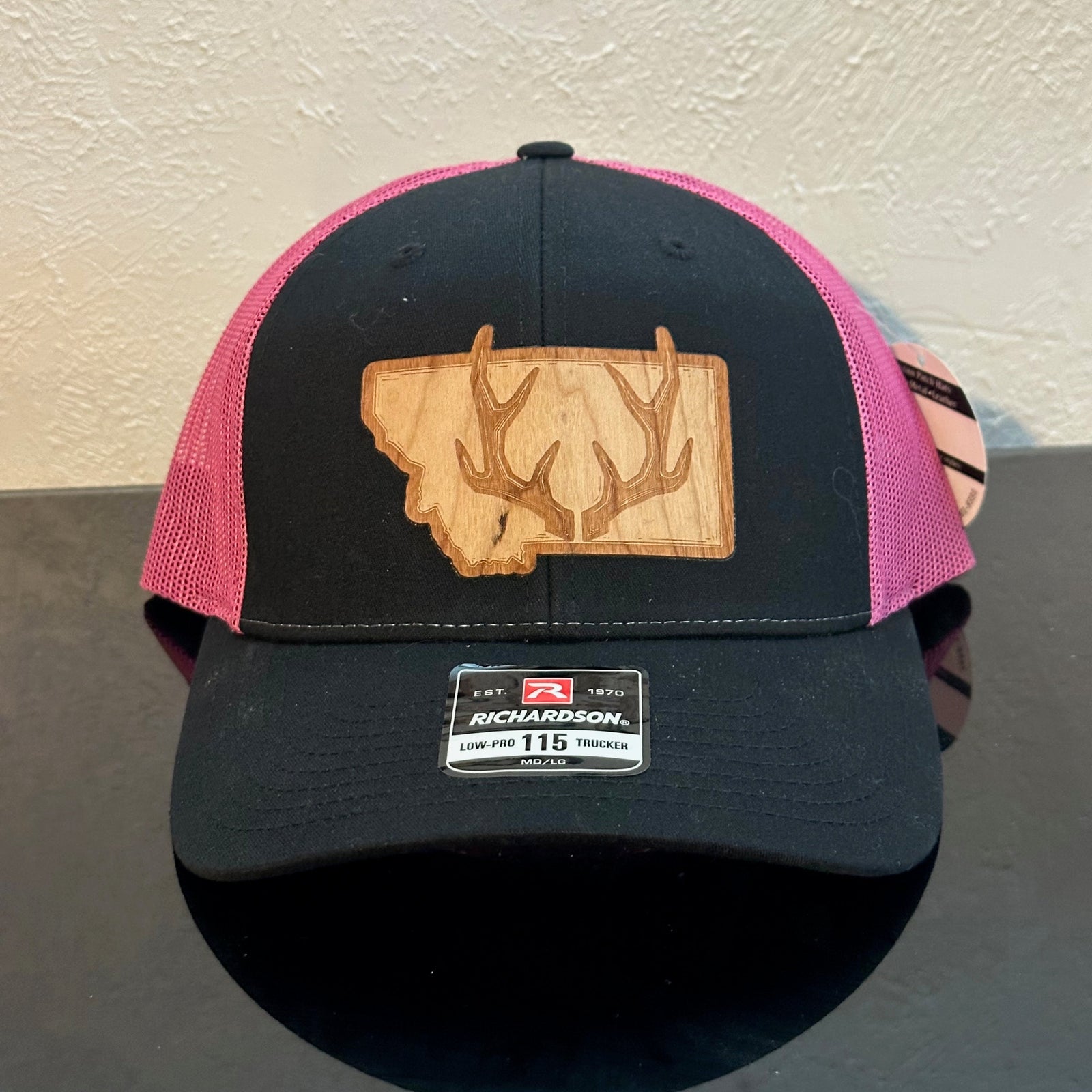 Front of a Richardson 115 Black & Pink trucker hat decorated with a Montana Antler Cherry Wood Patch - a pair of deer antlers superimposed on the state of Montana - made in Montana by Last Best Supply Co.