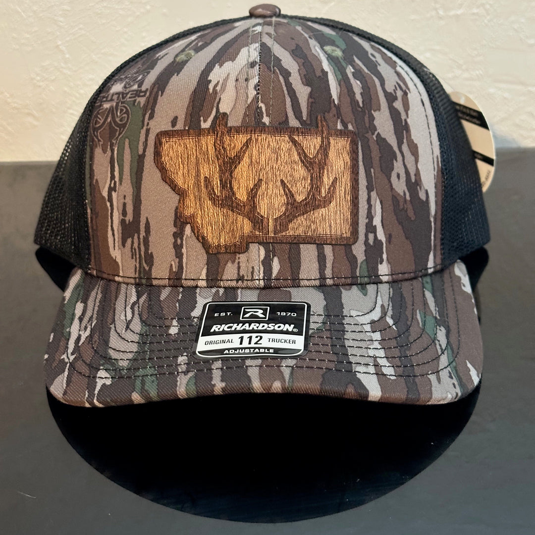 Front of a Richardson 112 Realtree Camo trucker hat decorated with a Montana Antler Mahogany Wood Patch- a pair of deer antlers superimposed on the state of Montana - made in Montana by Last Best Supply Co.