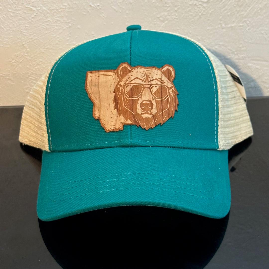 Front of an econscious Eco Trucker Teal & Cream trucker hat decorated with a Montana Bear Cherry Wood Patch - a bear head wearing sunglasses superimposed on the state of Montana - made in Montana by Last Best Supply Co.