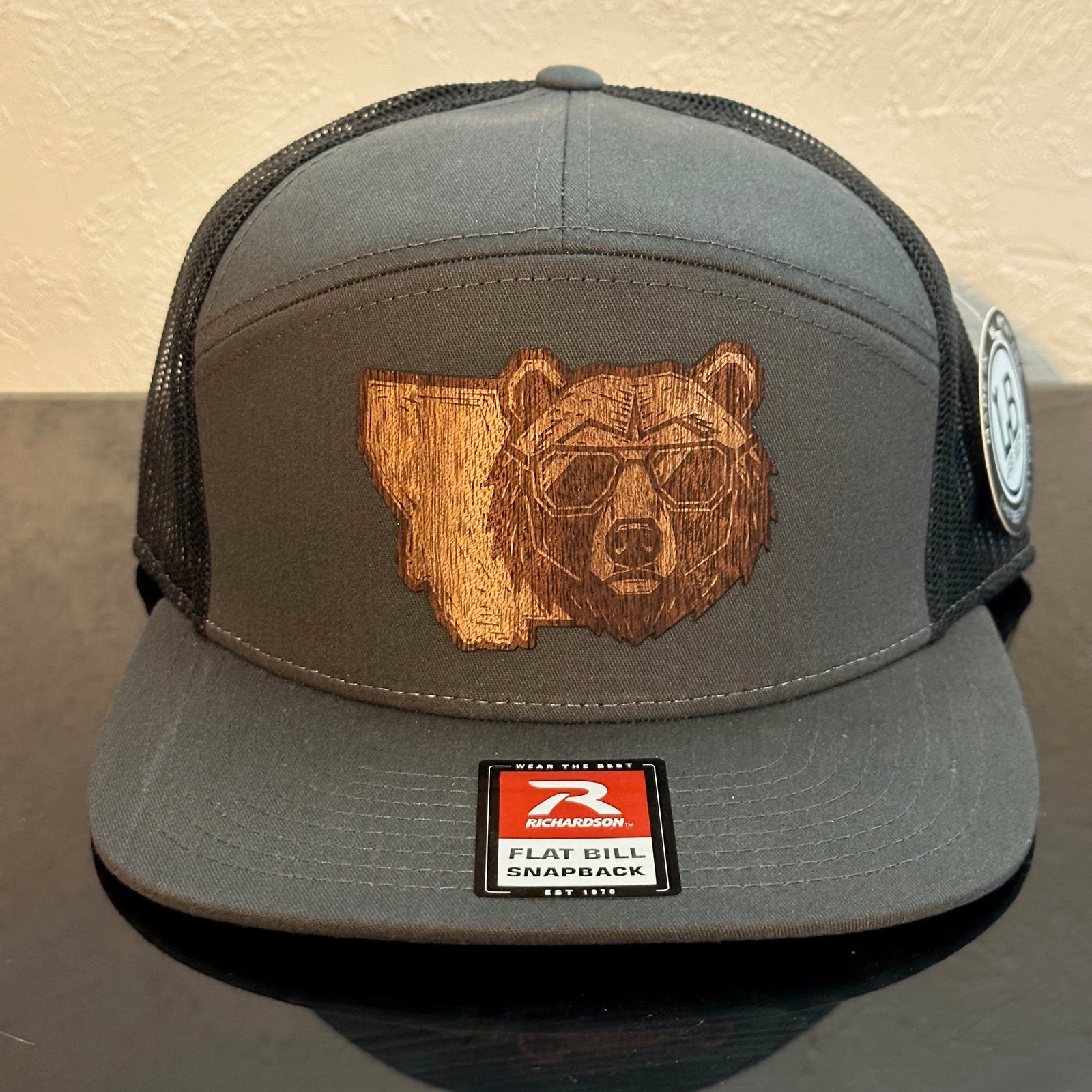 Front of a Richardson 168 Charcoal 7-Panel trucker hat decorated with a Montana Bear Mahogany Wood Patch - a bear’s head with sunglasses superimposed on the state of Montana - made in Montana by Last Best Supply Co.