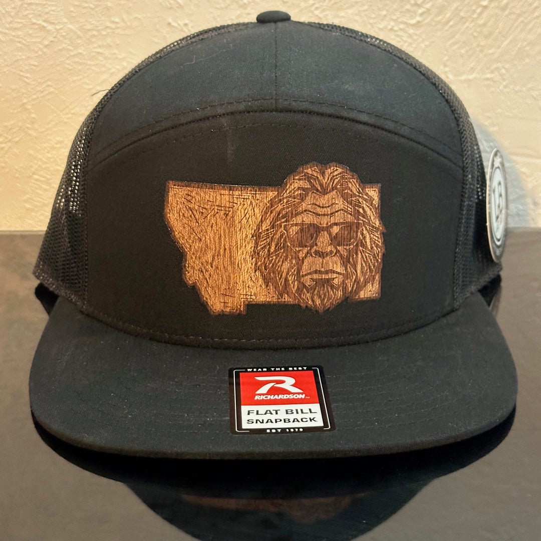 Front of a black Richardson 168 Black 7-Panel trucker hat decorated with a Montana Bigfoot Mahogany Wood Patch - Bigfoot’s head with sunglasses superimposed on the state of Montana - made in Montana by Last Best Supply Co.