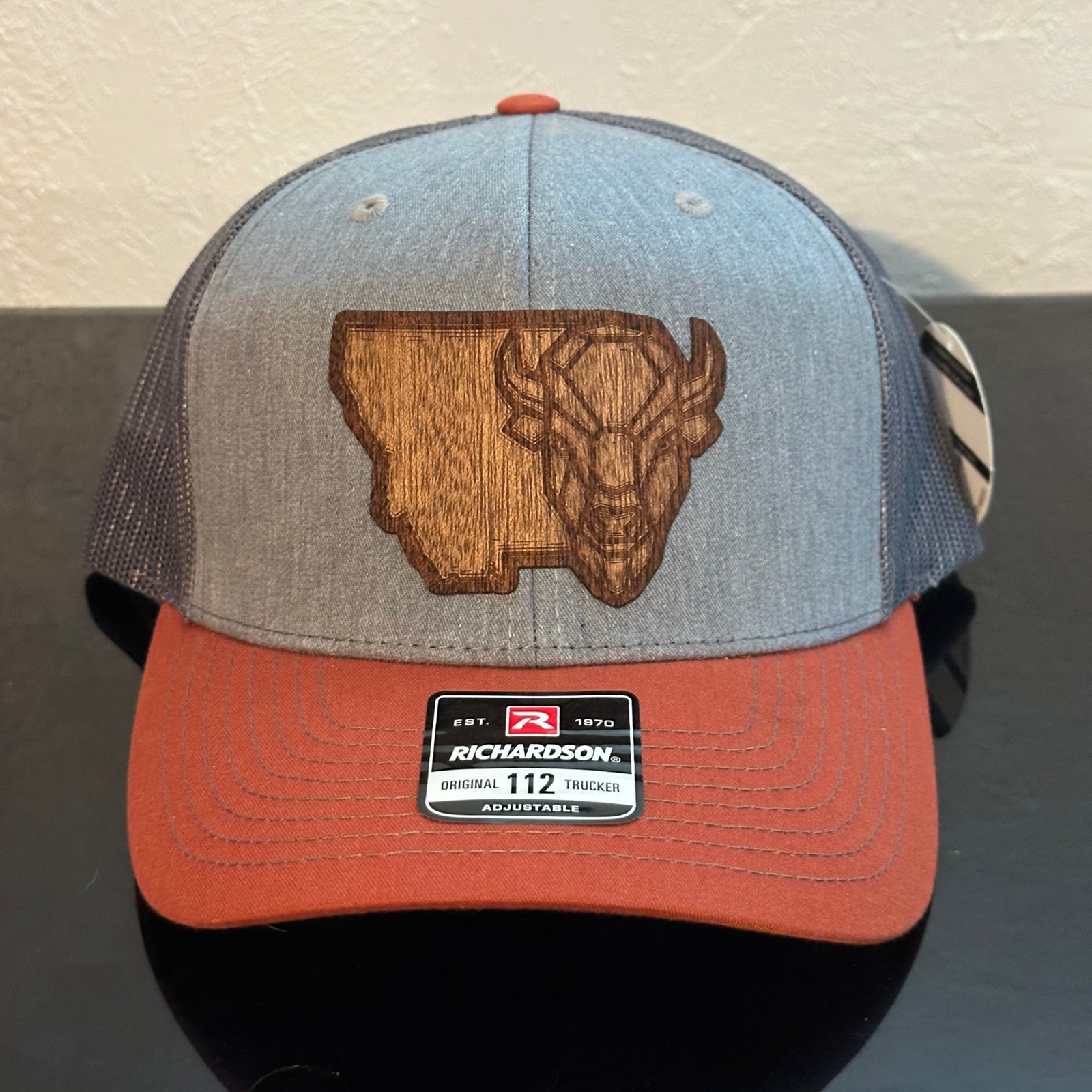 Front of a Richardson 112 Realtree Camo trucker hat decorated with a Montana Bison Mahogany Wood Patch - a geometric bison head superimposed on the state of Montana - made in Montana by Last Best Supply Co.