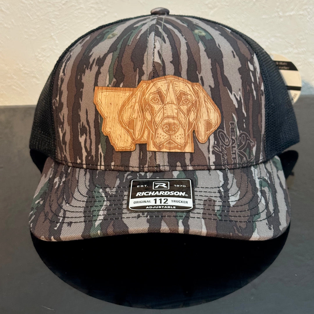 Front of a Richardson 112 Realtree Camo trucker hat decorated with a Montana Dog Cherry Wood Patch - a geometric dog head superimposed on the state of Montana - made in Montana by Last Best Supply Co.