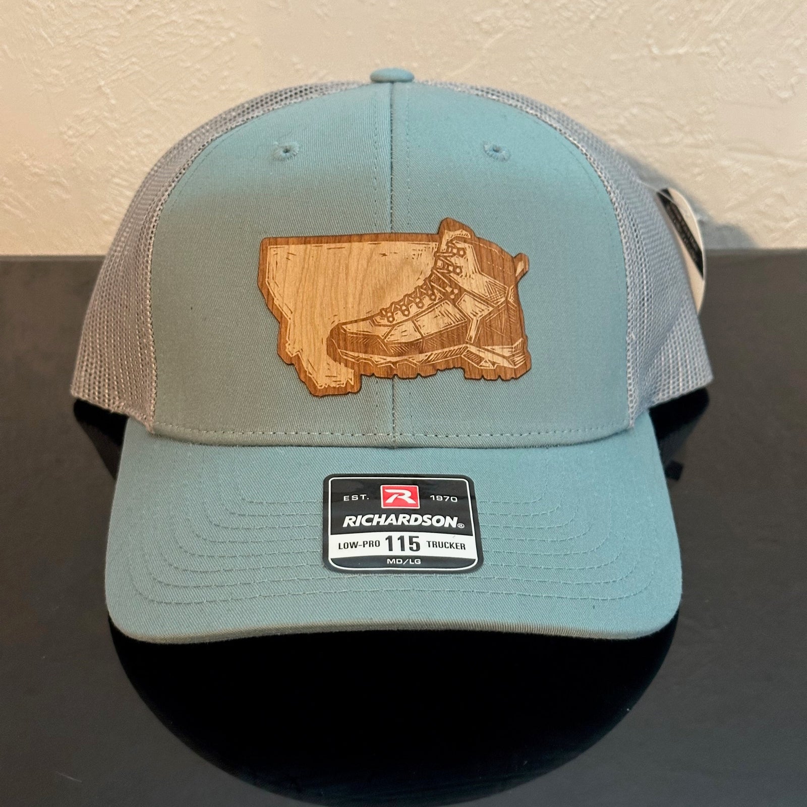 Front of a Richardson Richardson 115 Smoke Blue & Grey Mesh trucker hat decorated with a Montana Hiking Boot Cherry Wood Patch - a sketch of a hiking boot superimposed on the state of Montana - made in Montana by Last Best Supply Co.