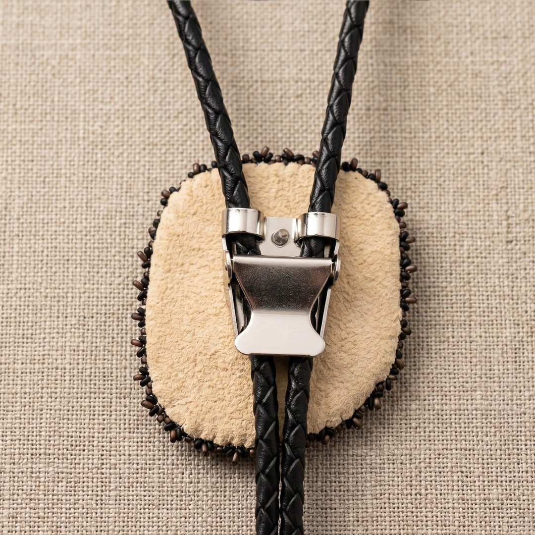 Bolo tie with leather and metal clasp on a beige fabric background
