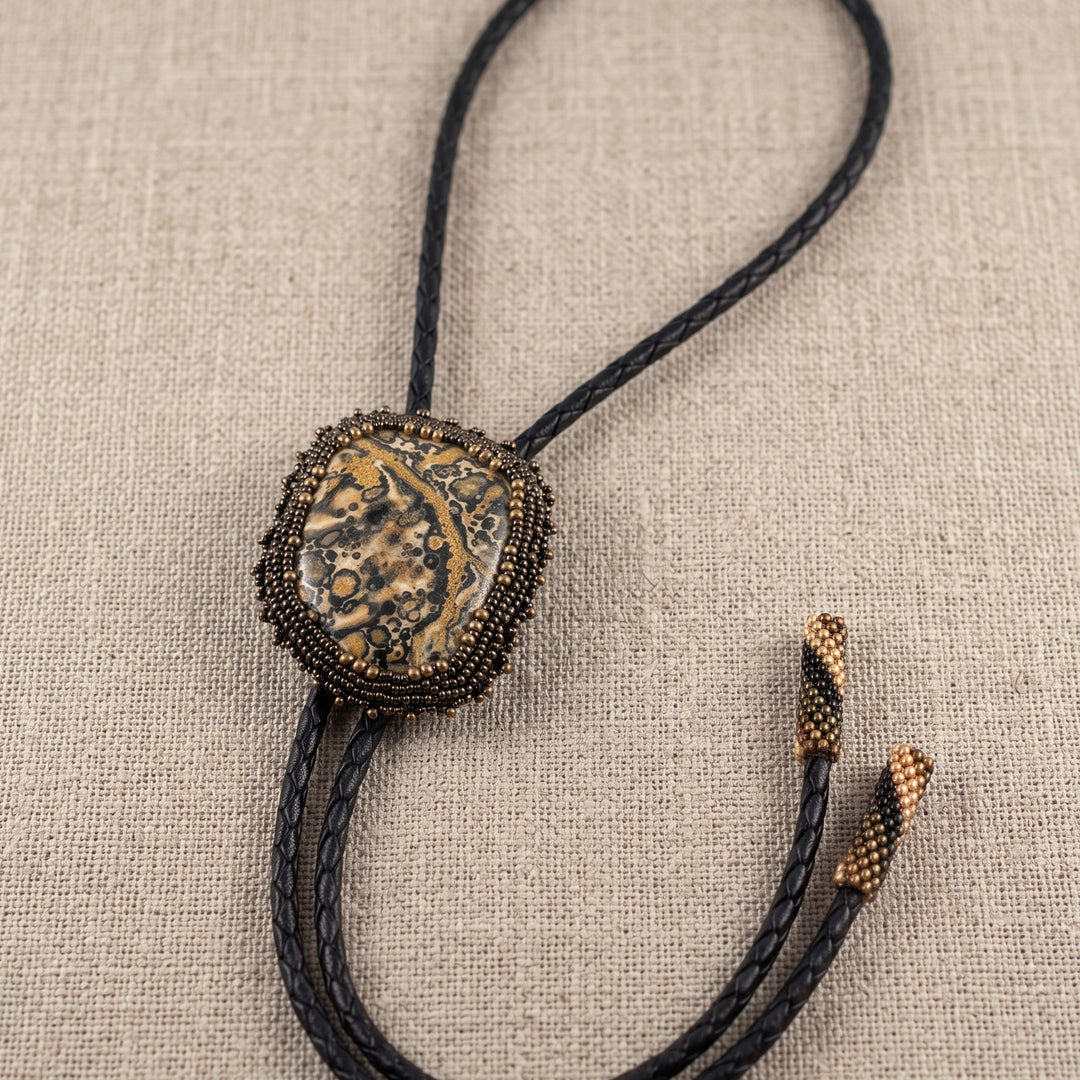Bolo tie with decorative leopard jasper stone and braided leather on a beige fabric background