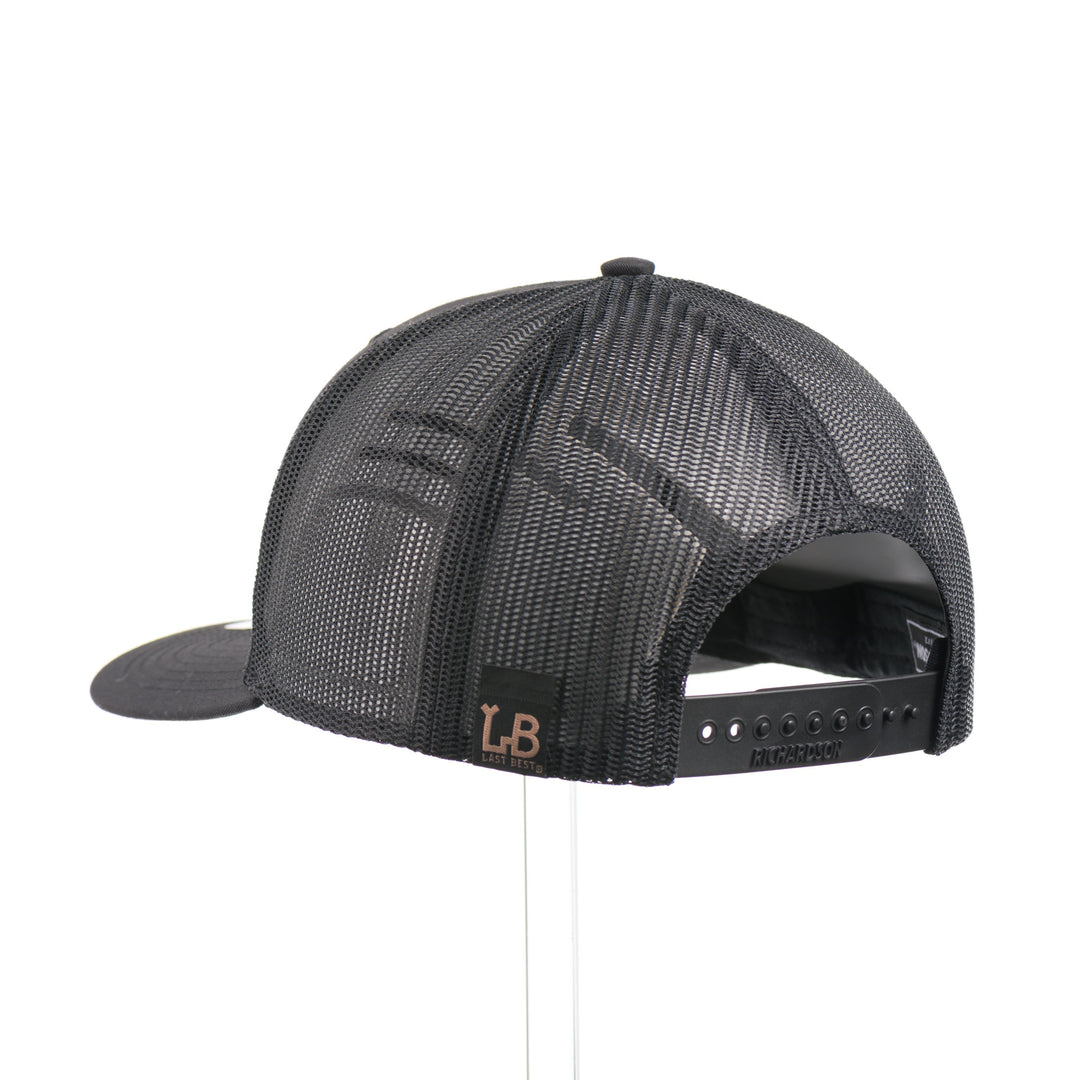 The back of a black Richardson trucker hat with an etched mahogany wood American flag and bear cut out on a black metal patch.
