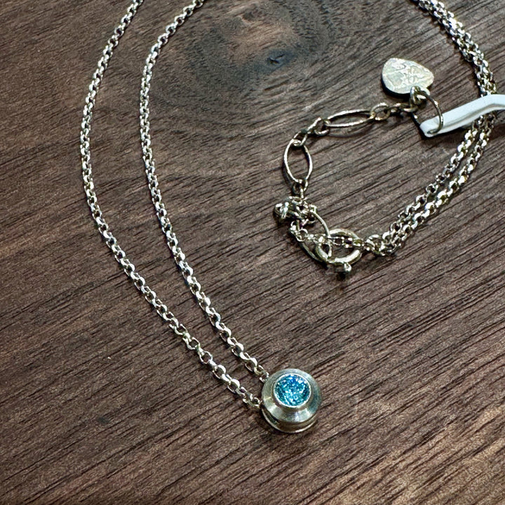 A cubic zirconia gemstone colored brilliant blue Aquamarine for a MarchBirthstone Necklace, set in sterling silver on a dark wood background