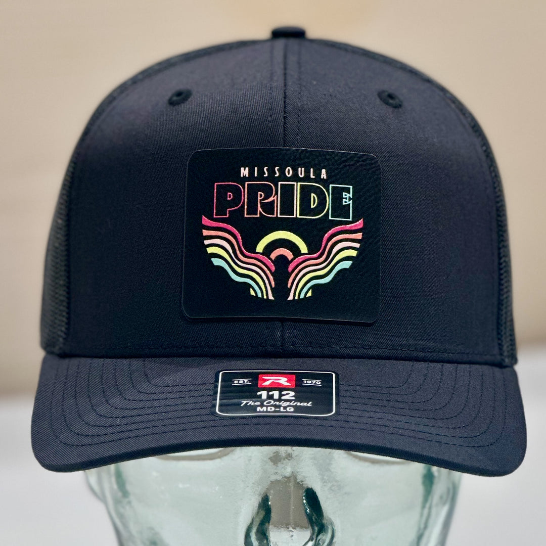 A richardson 112 black trucker hat with a leatherette patch of Missoula Pride&