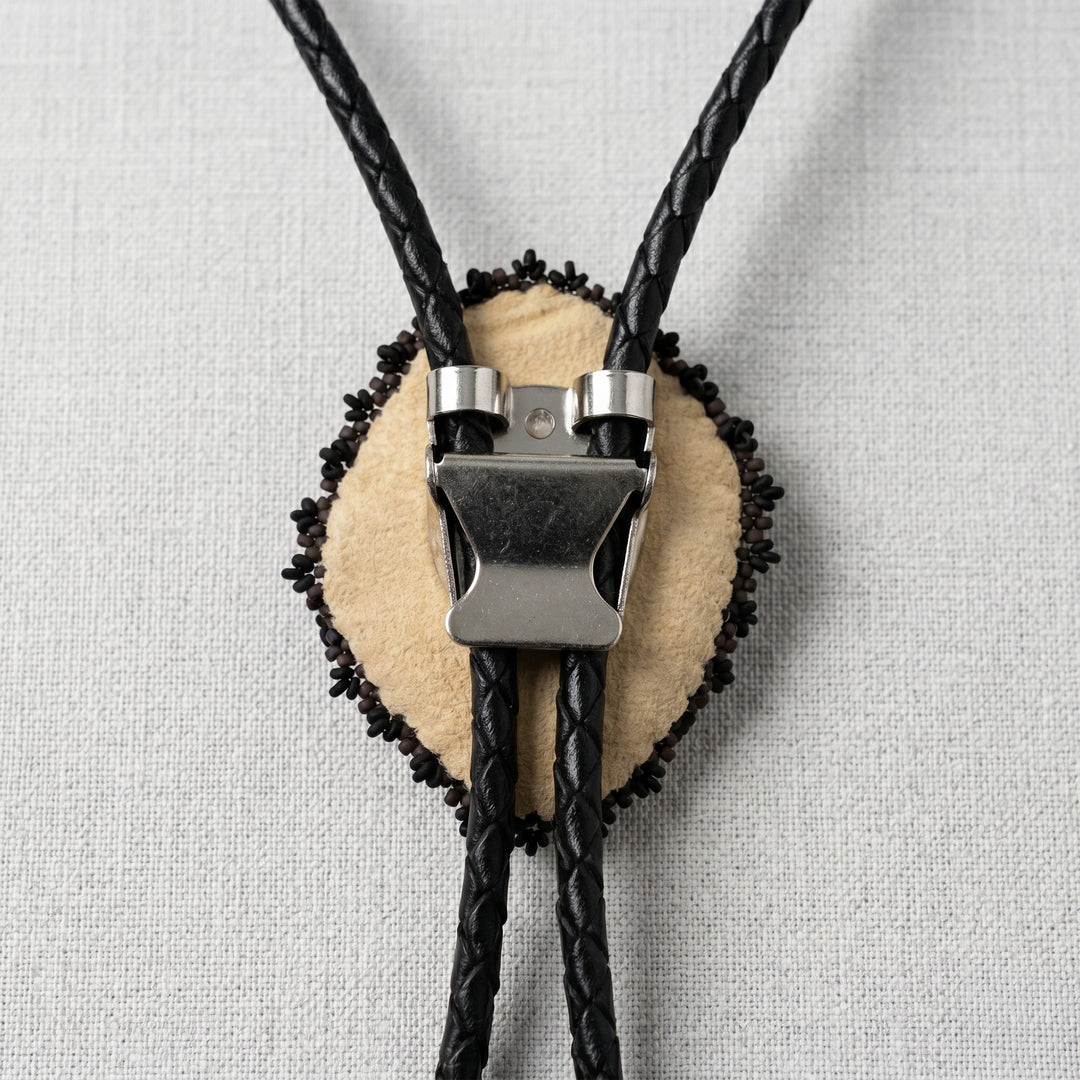 back of a Bolo tie with black braided cord and beige center on a light gray background