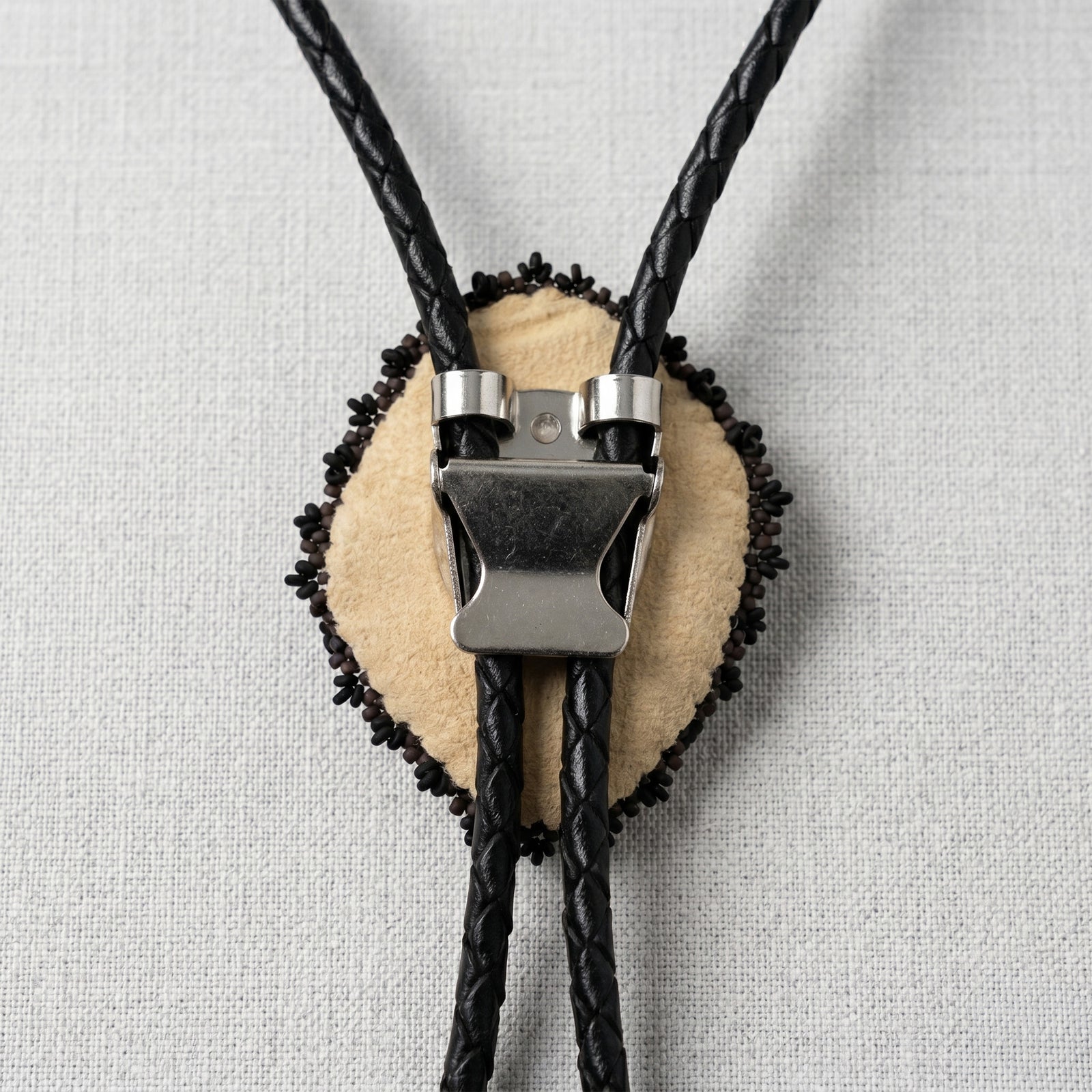 back of a Bolo tie with black braided cord and beige center on a light gray background