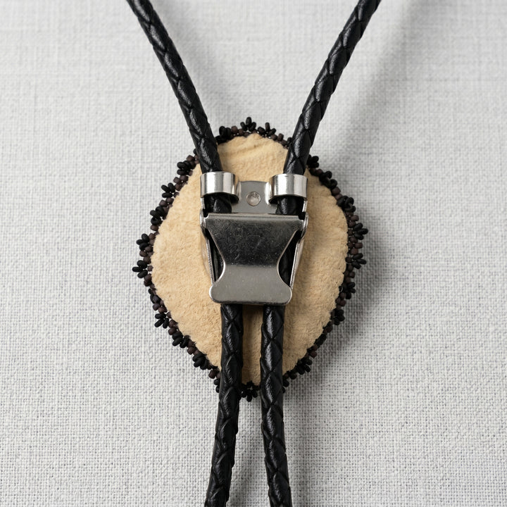 back of a Bolo tie with black braided cord and beige center on a light gray background