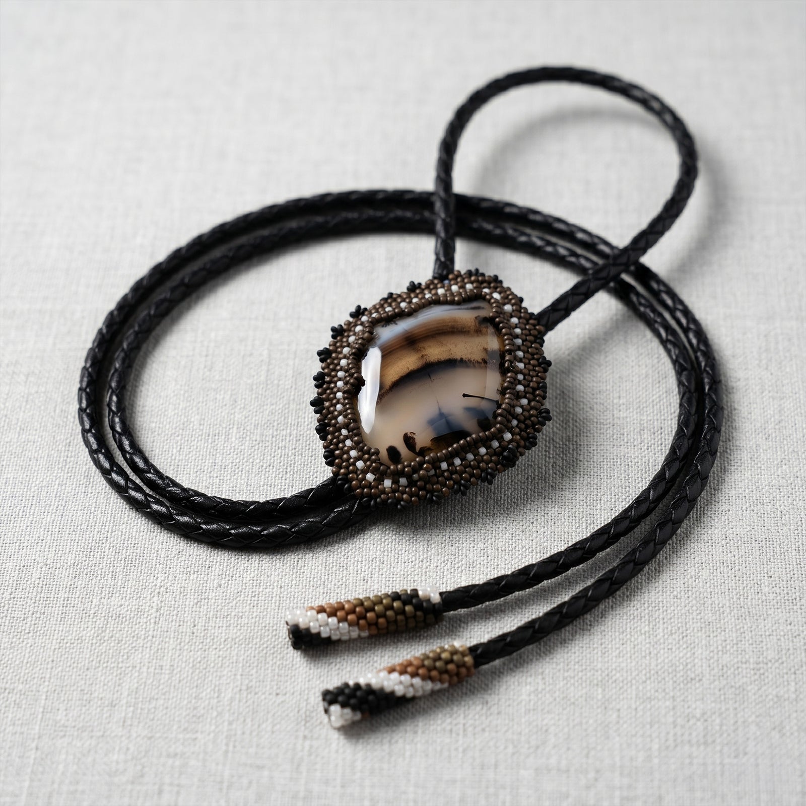 Bolo tie with agate stone and beaded tassels on a light fabric background