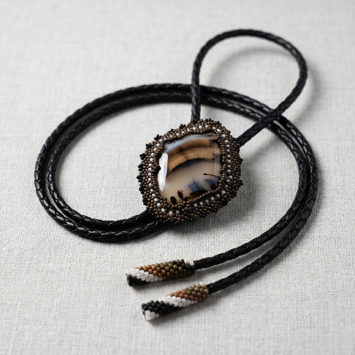Bolo tie with agate stone and beaded tassels on a light fabric background