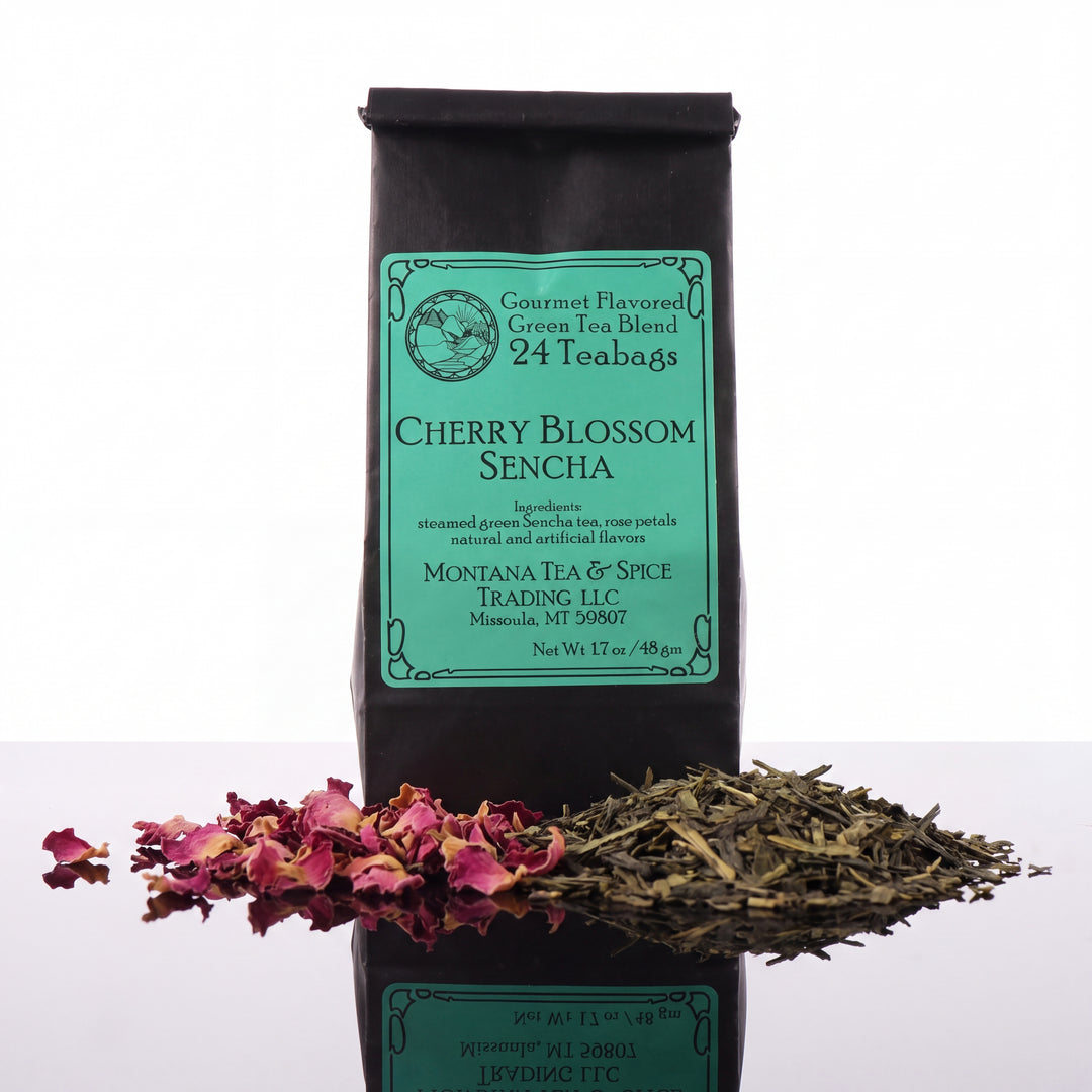 A black bag of Cherry Blossom Sencha green tea from Montana Tea &amp; Spice is shown against a white background, with loose dried tea leaves and pink flower petals arranged in front of the bag.