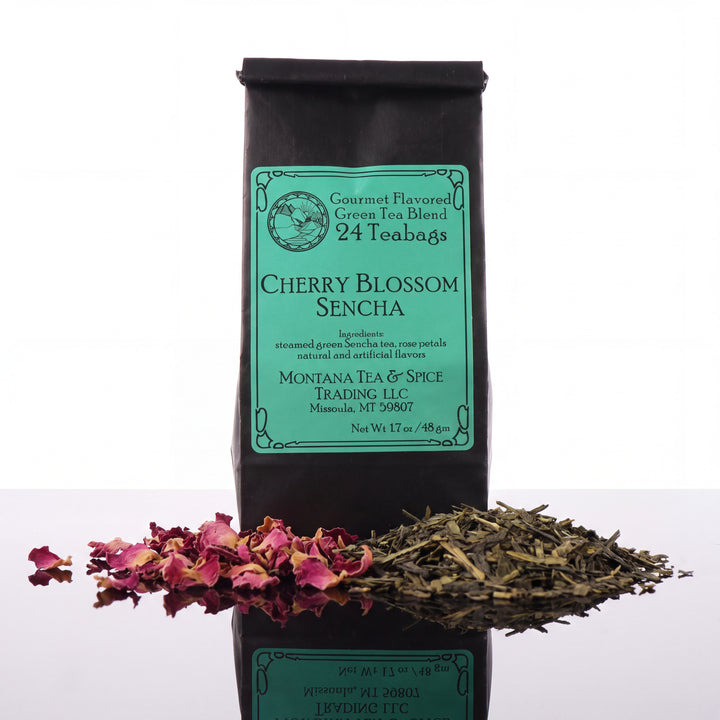 A black bag of Cherry Blossom Sencha green tea from Montana Tea &amp; Spice is shown against a white background, with loose dried tea leaves and pink flower petals arranged in front of the bag.