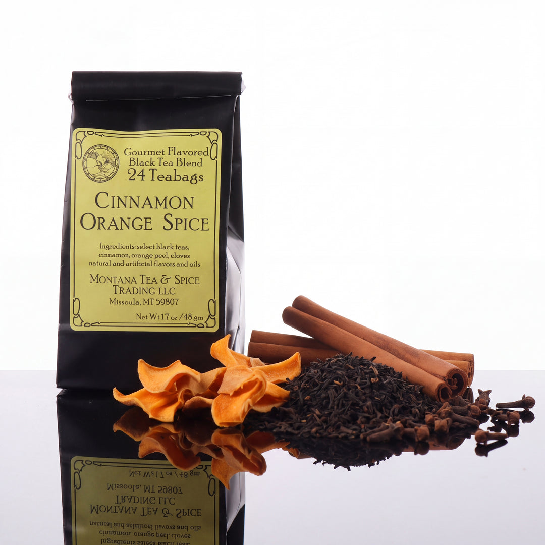 A black bag of tea with a yellow label reading Cinnamon Orange Spice with the tea ingredients next to the bag on a reflective surface.