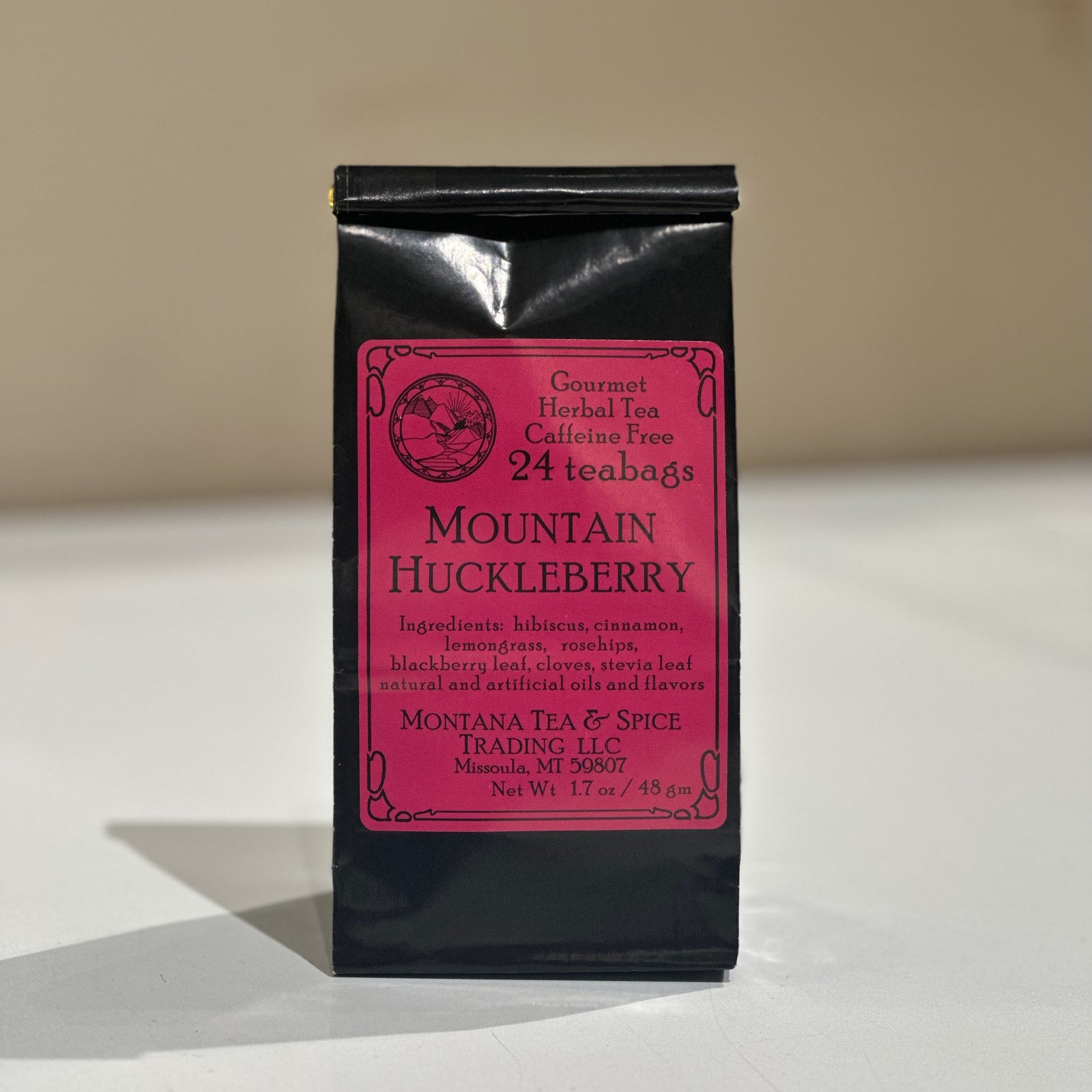 A black stand-up pouch of Mountain Huckleberry herbal tea by Montana Tea & Spice Trading LLC, featuring a pink label, set against a neutral beige background.