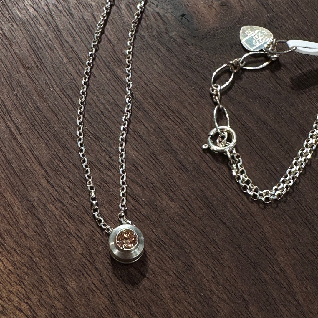 A cubic zirconia gemstone colored Topaz amber for a November Birthstone Necklace, set in sterling silver on a dark wood background