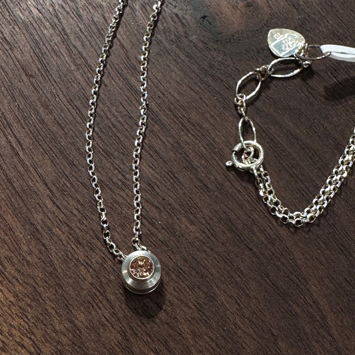 A cubic zirconia gemstone colored Topaz amber for a November Birthstone Necklace, set in sterling silver on a dark wood background