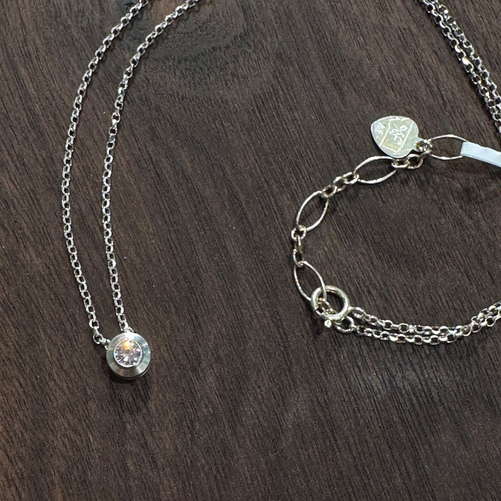 A cubic zirconia gemstone in a clear sparkling representation of an light pink tourmaline October Birthstone Necklace, set in sterling silver on a dark wood background