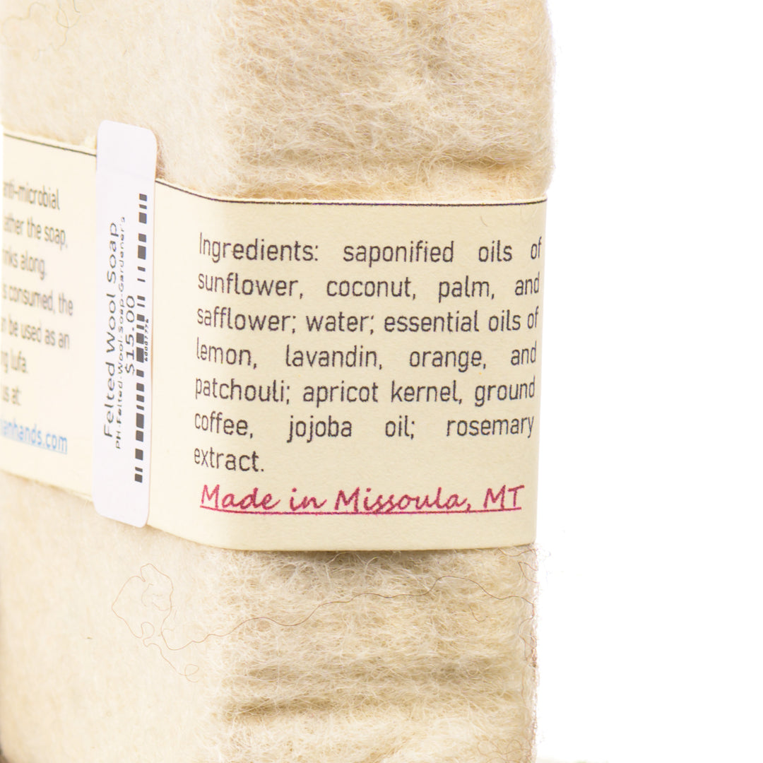 Close-up of a  wool felted soap bar with a label detailing ingredients and origin, on a white background. Made in Missoula