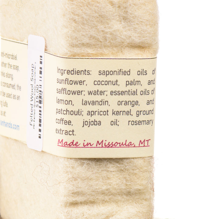Close-up of a  wool felted soap bar with a label detailing ingredients and origin, on a white background. Made in Missoula