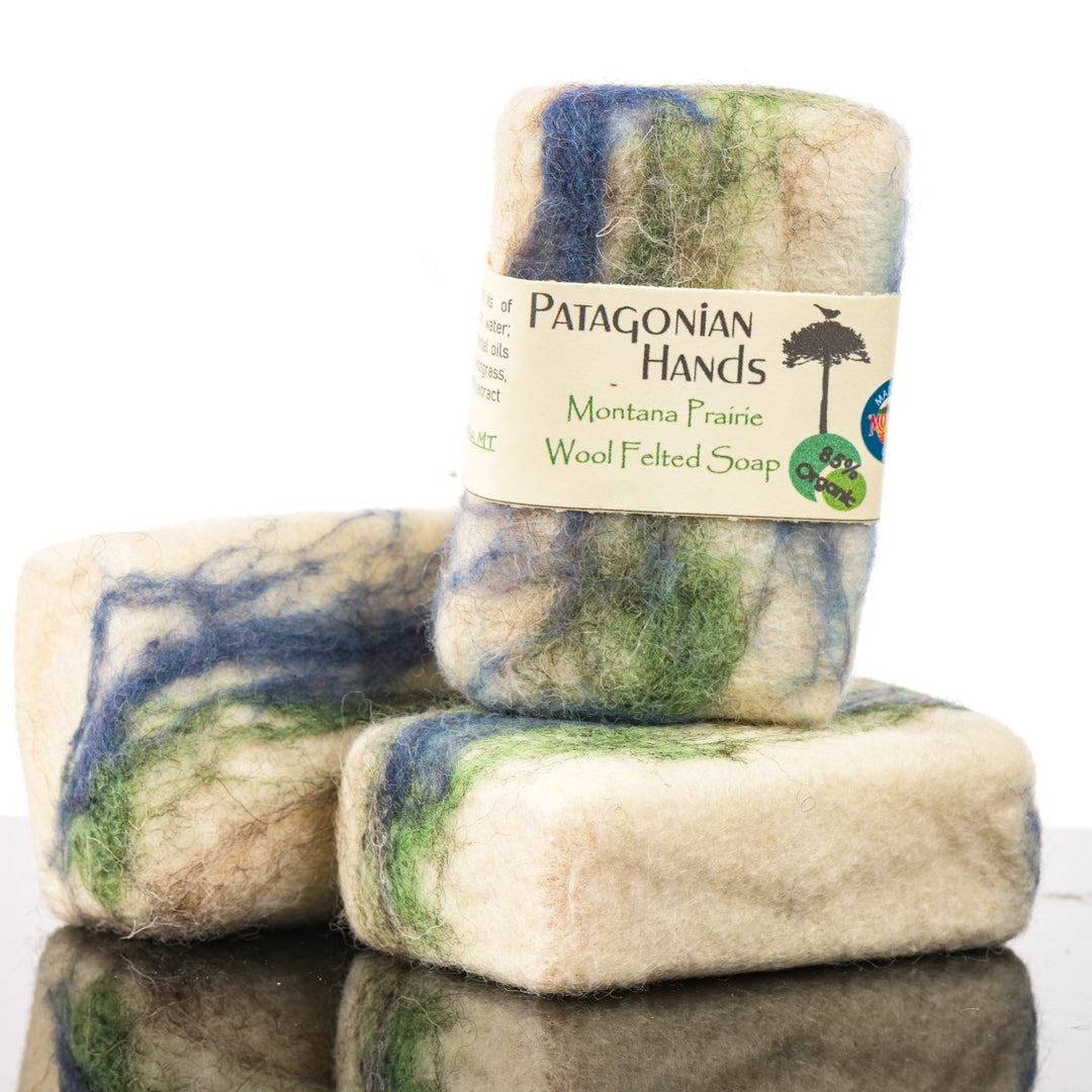 Three pieces of Patagonian Hands Montana Prairie wool felted soap stacked on a reflective surface with a white background.