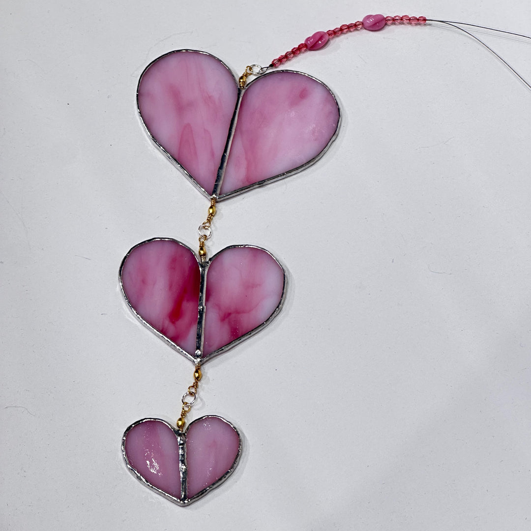 A stained glass suncatcher with three pink marbled glass heart panels with a pink beaded cord 