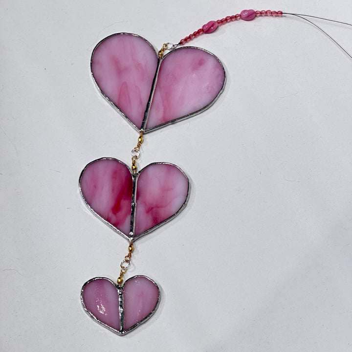 A stained glass suncatcher with three pink marbled glass heart panels with a pink beaded cord 
