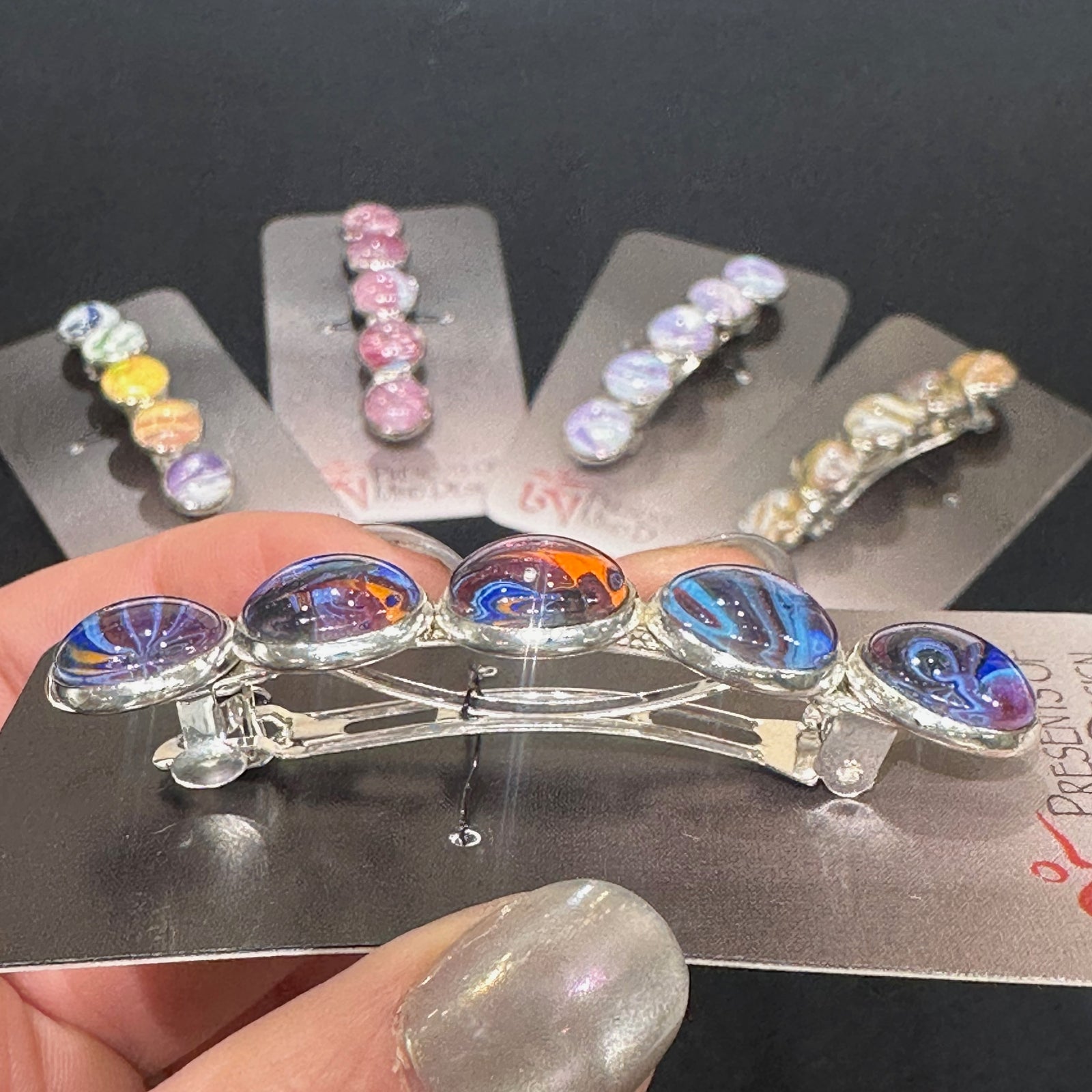 Side view of a stainless steel barrette with swirling acrylic pour and glass cabochons made in Montana
