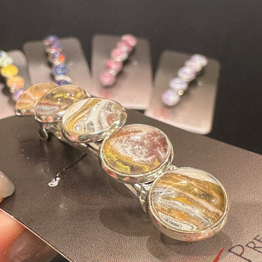 A close up of the detail on a stainless steel barrette with swirling gold, copper and silver acrylic paint and glass cabachons