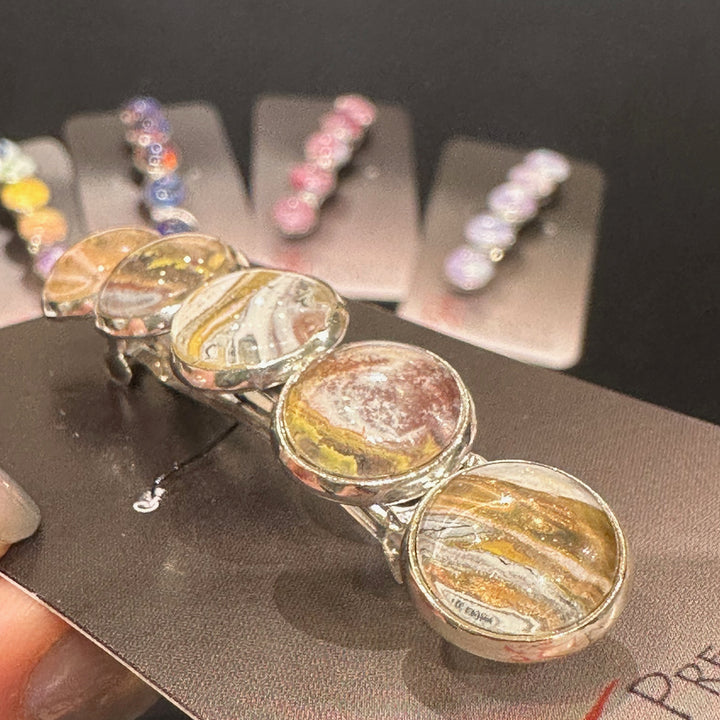 A close up of the detail on a stainless steel barrette with swirling gold, copper and silver acrylic paint and glass cabachons