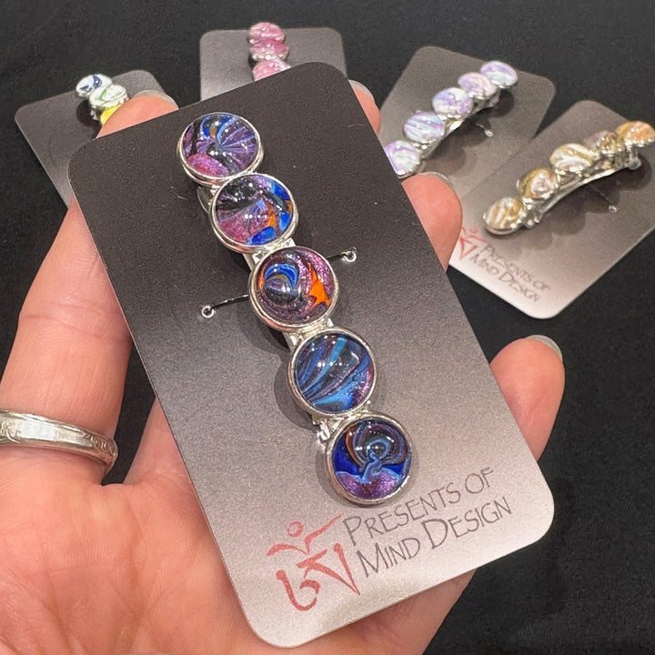 A stainless steel barrette featuring rich blue purple and orange paint swirls under glass cabachons