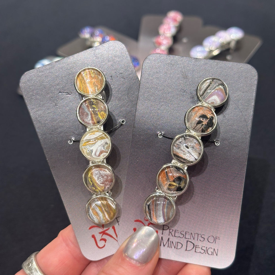 Two barrettes featuring gold, copper, black and white paint swirls under glass cabachons.