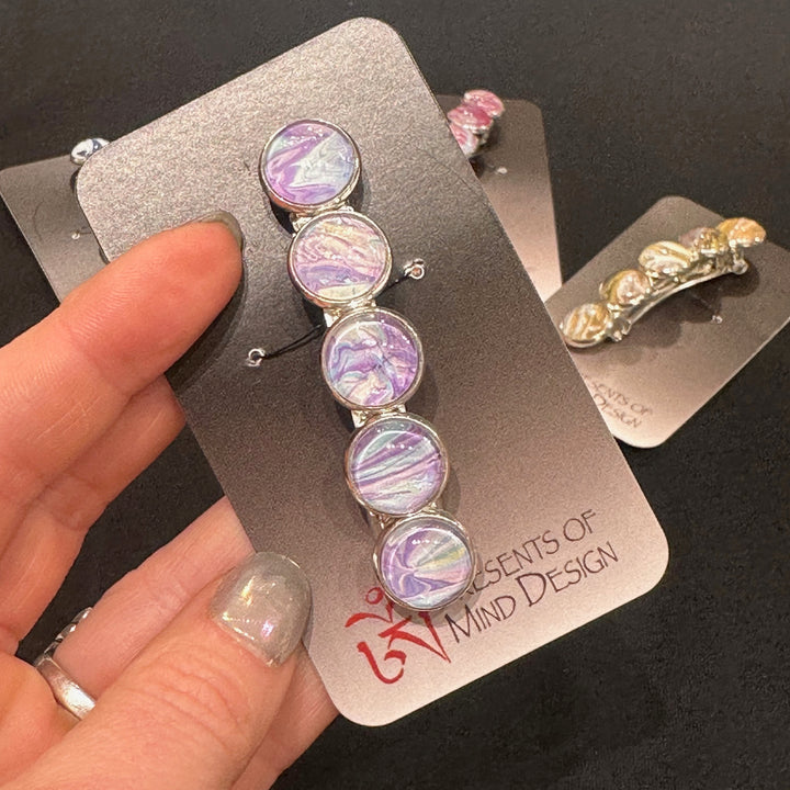 A stainless steel barrette with purple, blue and white paint swirled under glas cabachons