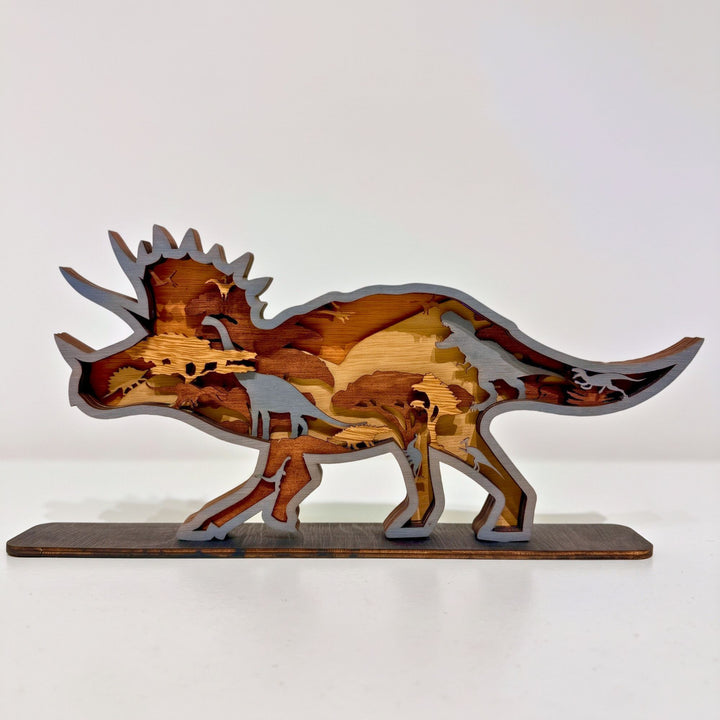 Multiple layers of natural wood are precision laser-cut and hand-assembled to form a dynamic Triceratops silhouette, revealing intricate prehistoric scenes and silhouettes hidden within every tier. Mounted on a sturdy display base, this freestanding wooden sculpture