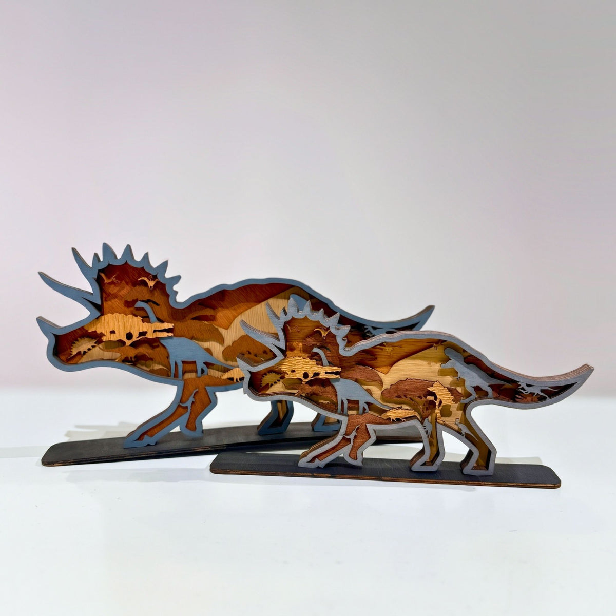 Multiple layers of natural wood are precision laser-cut and hand-assembled to form a dynamic Triceratops silhouette, revealing intricate prehistoric scenes and silhouettes hidden within every tier. Mounted on a sturdy display base, this freestanding wooden sculpture