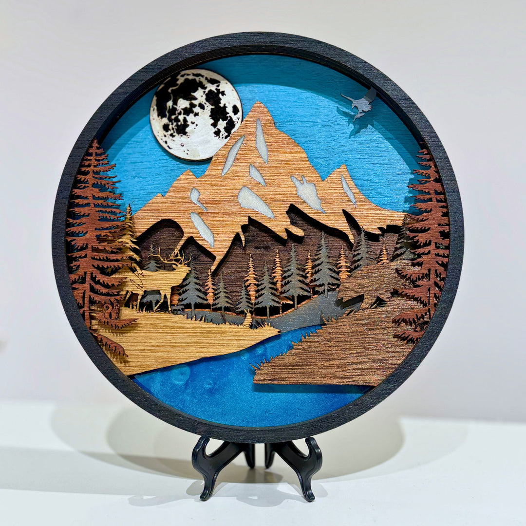 Layer upon layer of laser-cut wood is stacked by hand to build a scene of mountain peaks, forest and a winding river, with real depth that shifts as the light changes through the day.