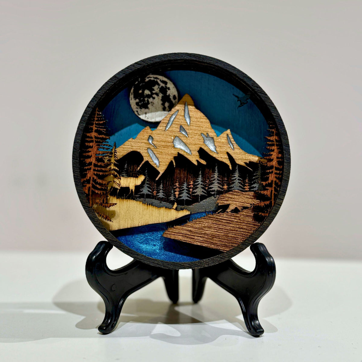 Layer upon layer of laser-cut wood is stacked by hand to build a scene of mountain peaks, forest and a winding river, with real depth that shifts as the light changes through the day.