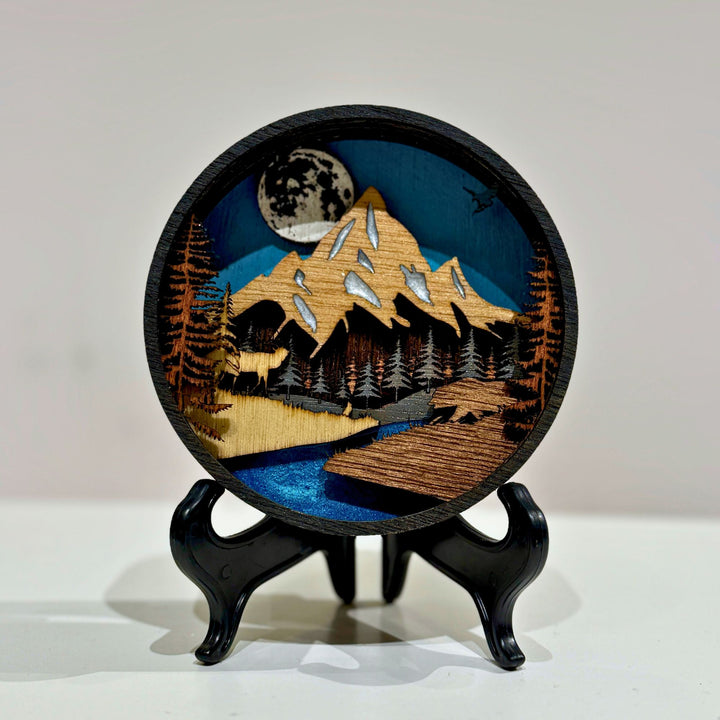 Layer upon layer of laser-cut wood is stacked by hand to build a scene of mountain peaks, forest and a winding river, with real depth that shifts as the light changes through the day.