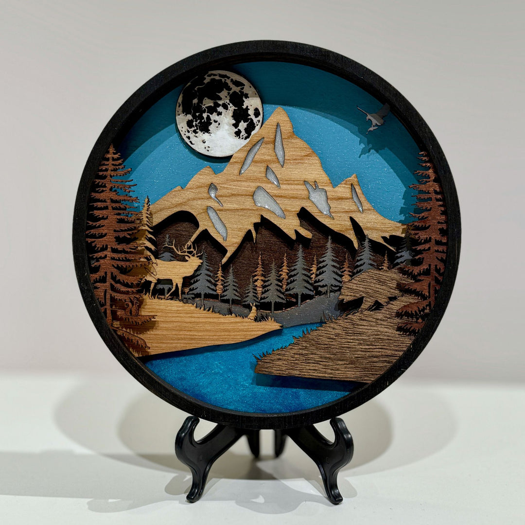 Layer upon layer of laser-cut wood is stacked by hand to build a scene of mountain peaks, forest and a winding river, with real depth that shifts as the light changes through the day.