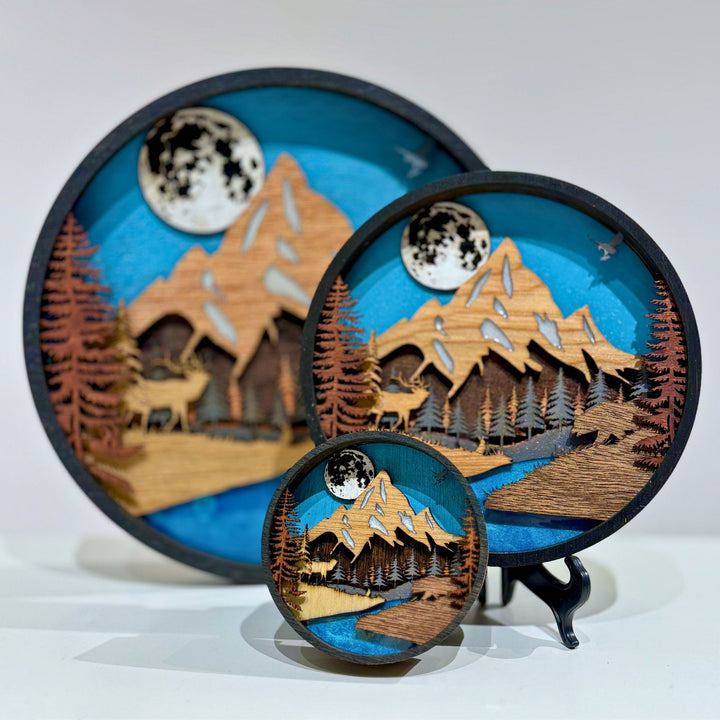 Layer upon layer of laser-cut wood is stacked by hand to build a scene of mountain peaks, forest and a winding river, with real depth that shifts as the light changes through the day.