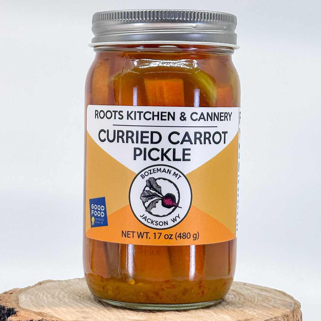 A 17oz jar of curried carrot pickles, with an orange label, by Roots Kitchen & Cannery in Bozeman Montana