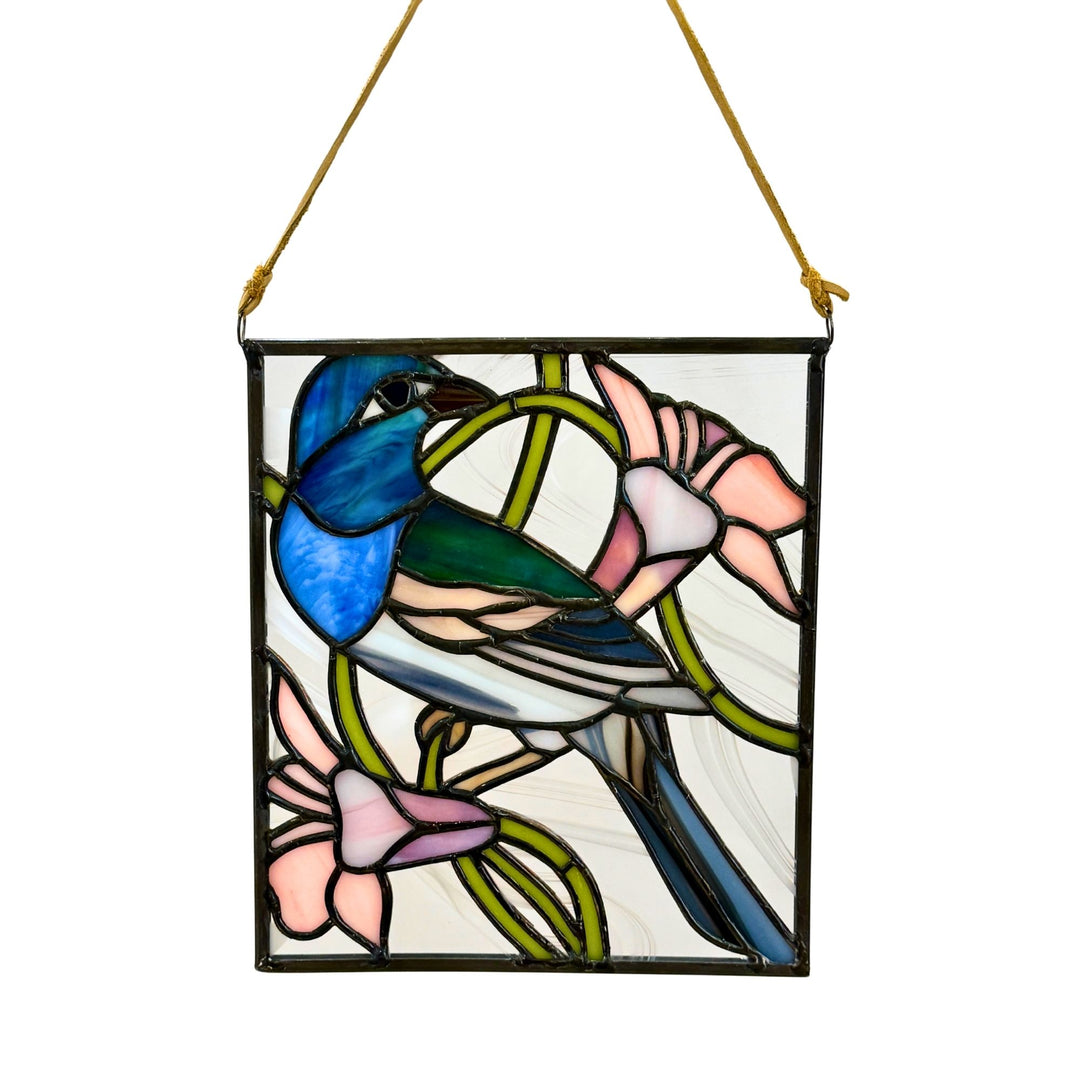 A square stained glass hanging panel featuring a bluebird perched among pink flowers and green leaves, suspended by a gold cord against a white background.