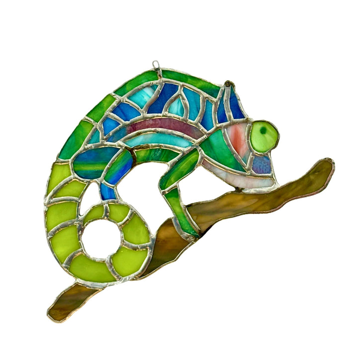 A stained glass suncatcher shaped like a chameleon perched on a branch, featuring vibrant green, blue, and yellow glass panels outlined in silver metal, isolated on a white background.