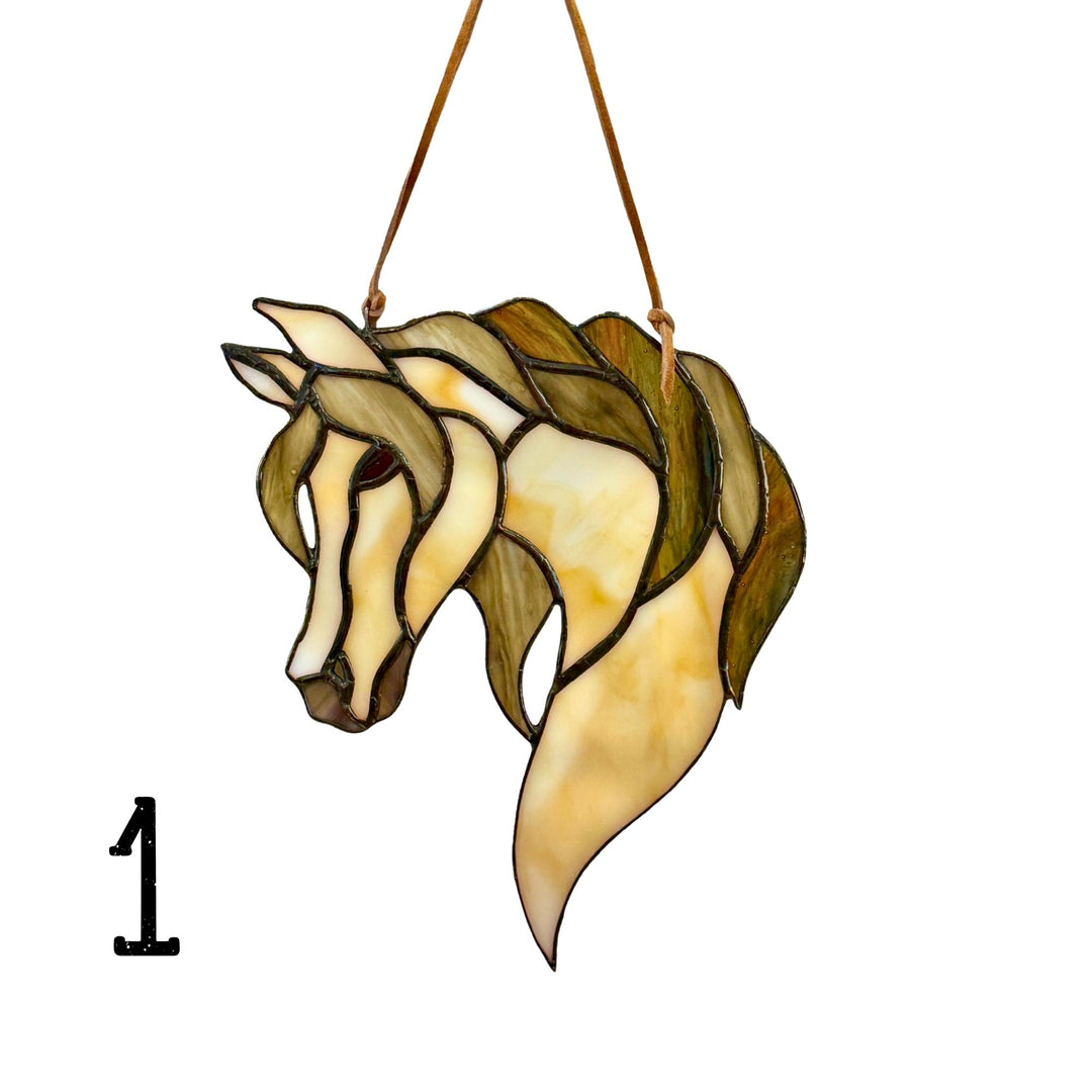 A stained glass hanging ornament shaped like a horse head, featuring cream, yellow, and olive green glass panels outlined in dark metal, suspended by two brown cords against a white background. A black number &